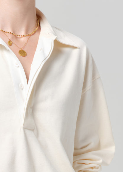 Person wearing a cream rugby with gold trim and light gray jeans on a plain background
