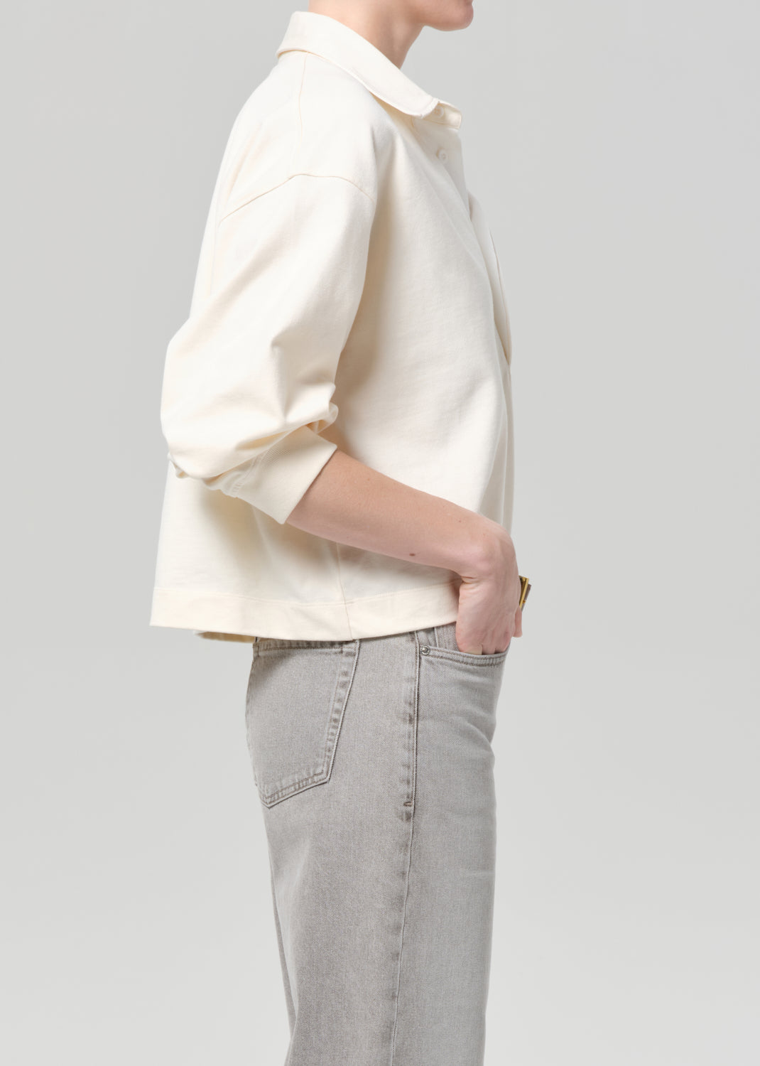 Person wearing a cream rugby with gold trim and light gray jeans on a plain background