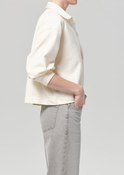 Person wearing a cream rugby with gold trim and light gray jeans on a plain background