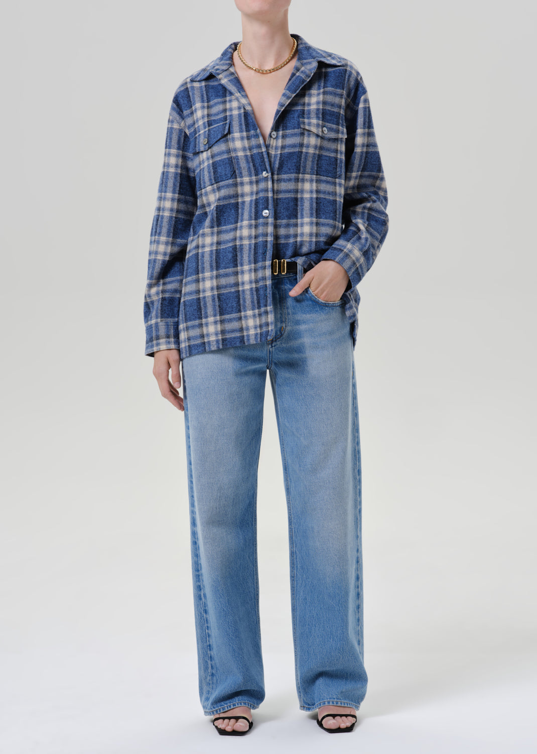 Person wearing a blue plaid button up shirt with light wash wide leg jeans and black sandals on a grey background
