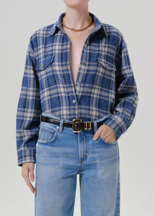 Person wearing a blue plaid button up shirt with light wash jeans on a grey background