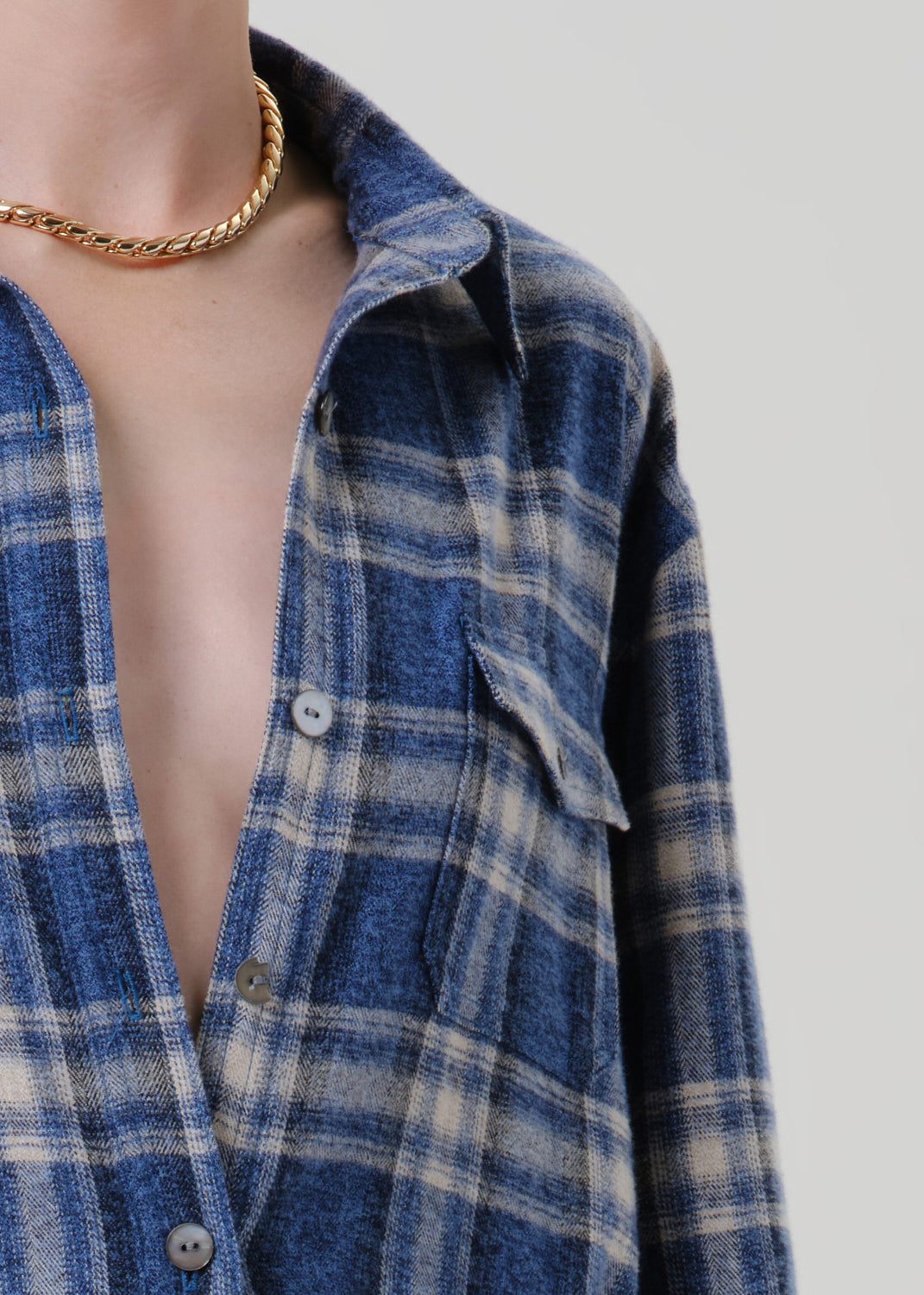 Person wearing a blue plaid button up shirt on a grey background