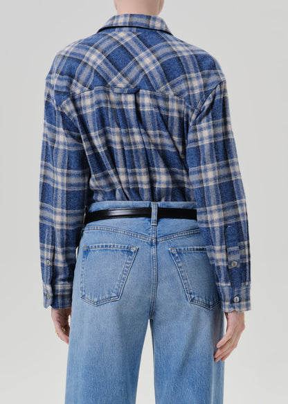 Person wearing a blue plaid button up shirt with light wash jeans viewed from the back on a grey background