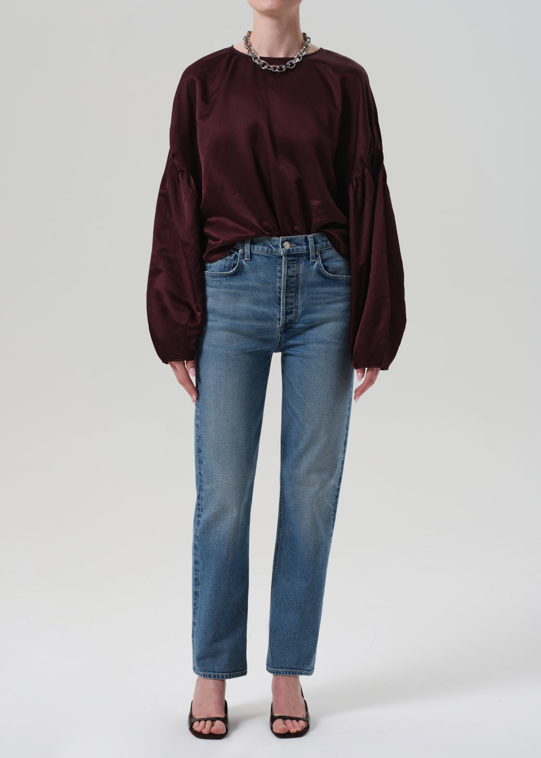 Person wearing a burgundy long-sleeve top and blue jeans on a plain background