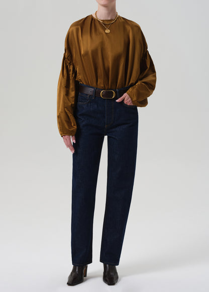 Person wearing a brown blouse with puffed sleeves and dark blue jeans on a plain background
