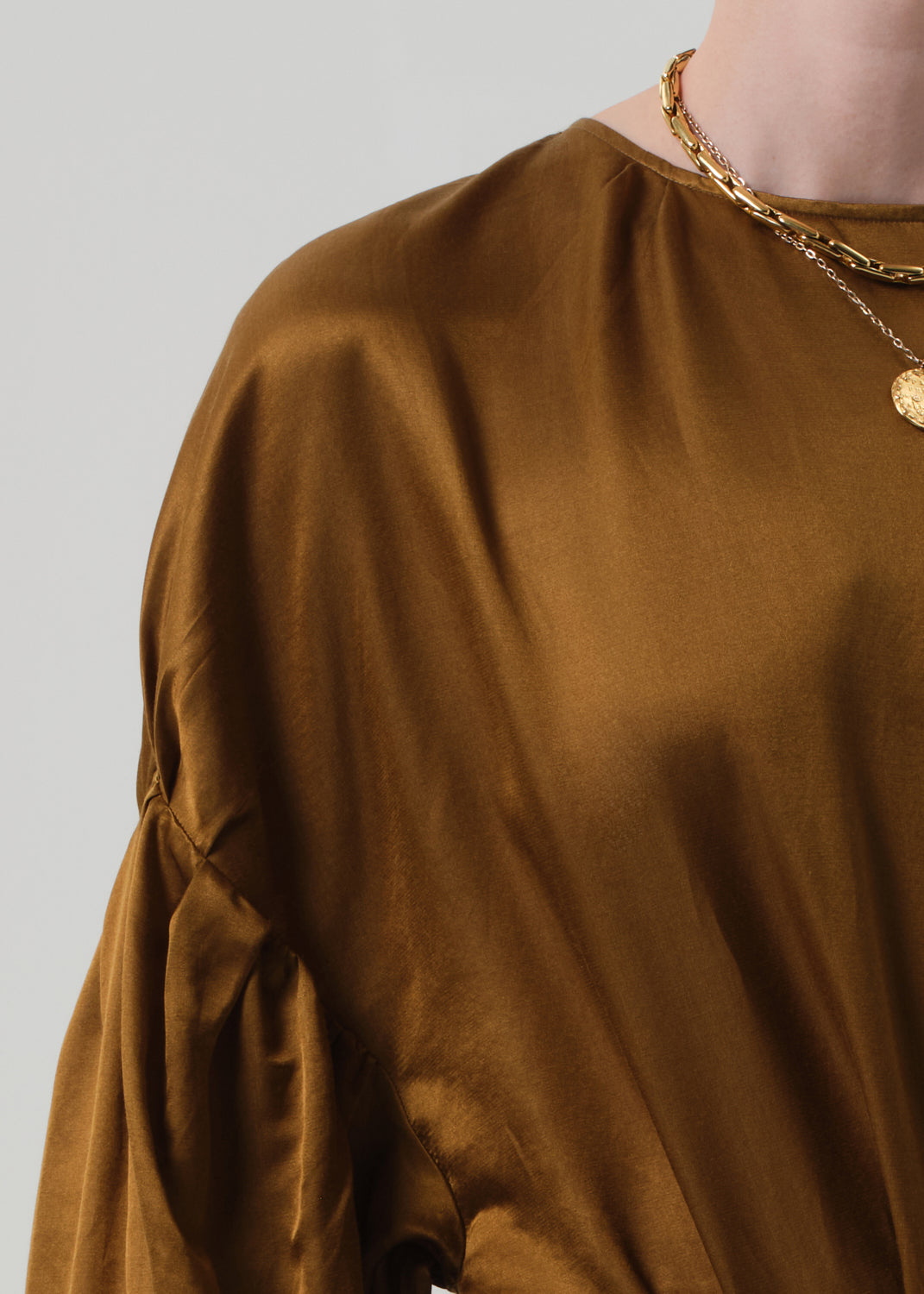 Person wearing a brown blouse with puffed sleeves and dark blue jeans on a plain background