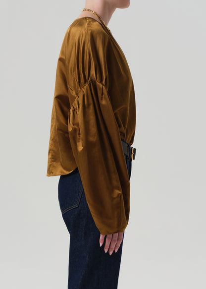 Person wearing a brown blouse with puffed sleeves and dark blue jeans on a plain background