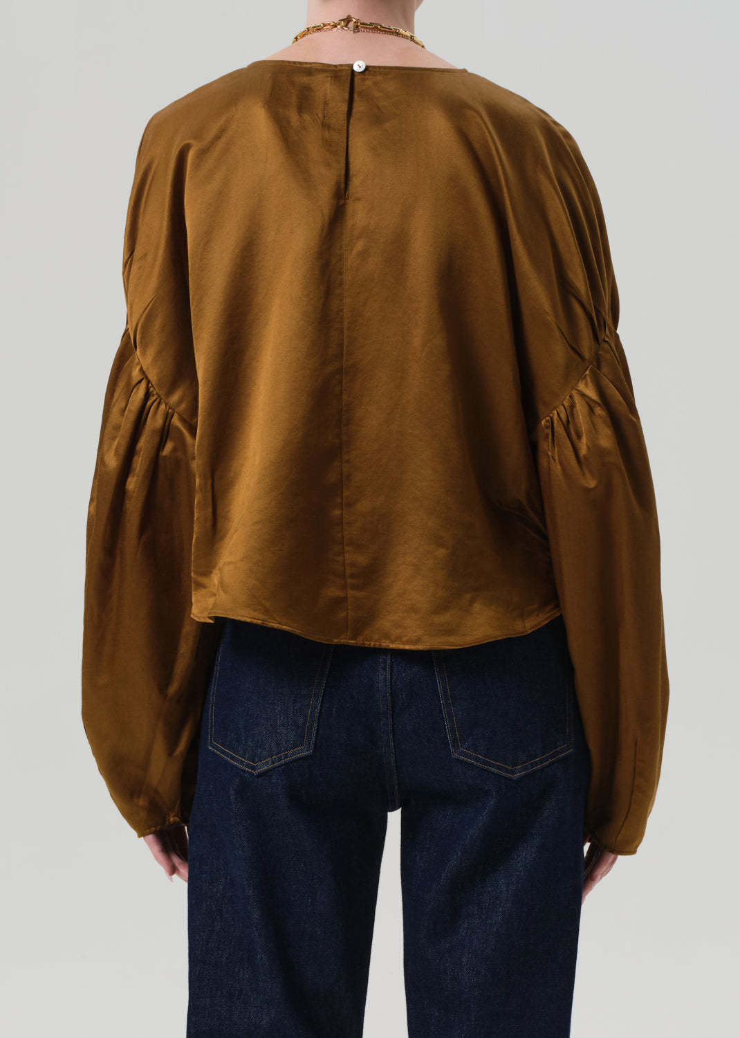 Person wearing a brown blouse with puffed sleeves and dark blue jeans on a plain background