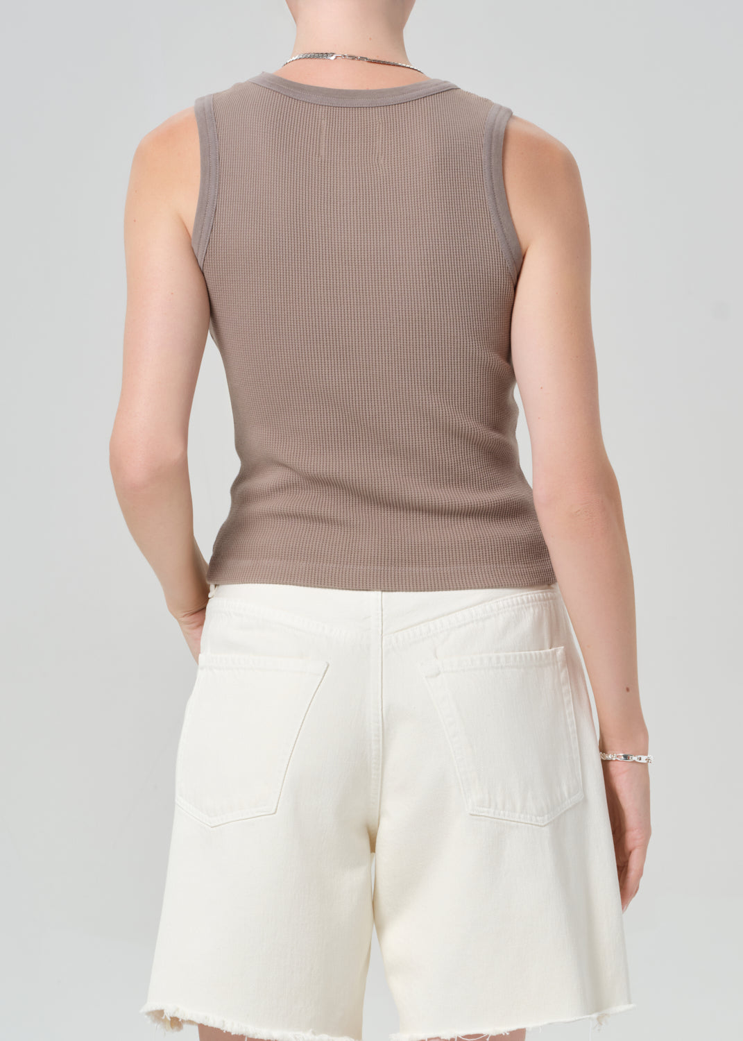 Person wearing a brown tank top and white shorts on a plain background