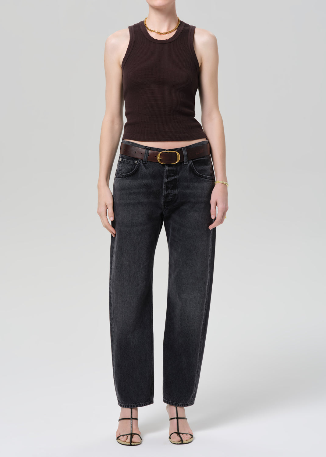 Person wearing a brown sleeveless top and black jeans on a gray background