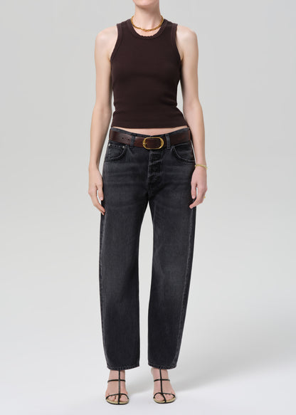 Person wearing a brown sleeveless top and black jeans on a gray background