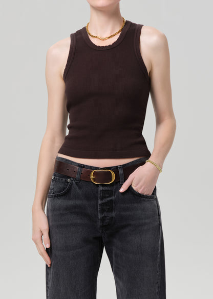 Person wearing a brown sleeveless top and black jeans on a gray background