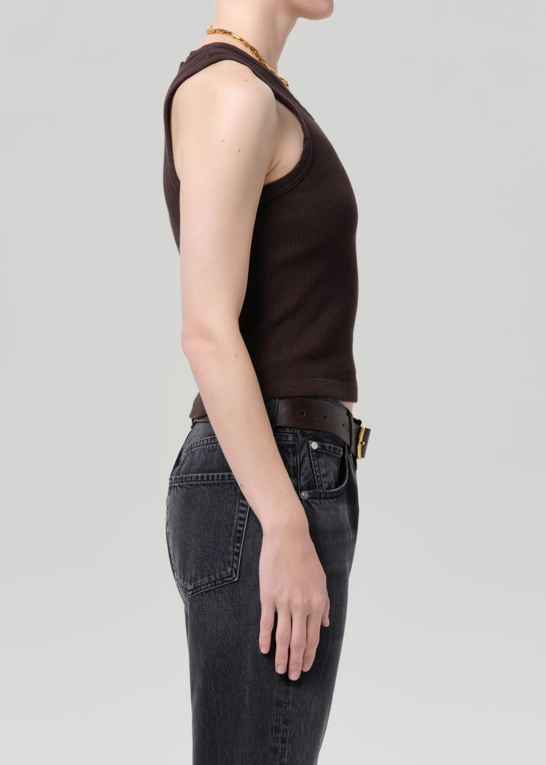 Person wearing a brown tank top and black jeans on a light gray background