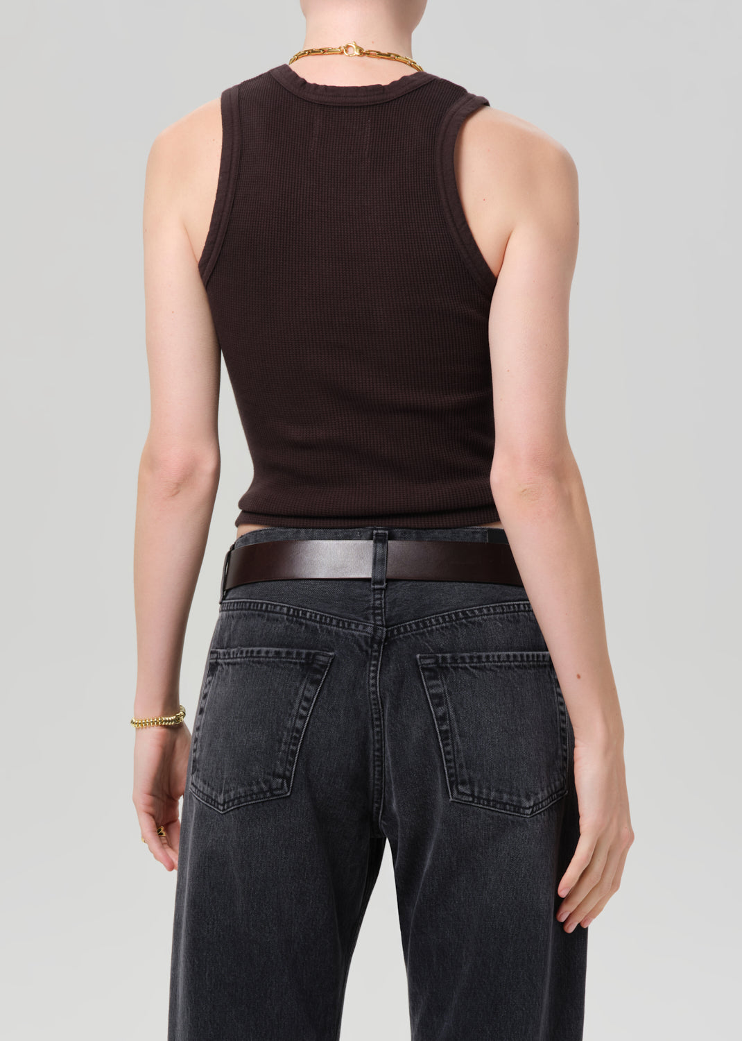 Person wearing a brown sleeveless top and black jeans on a gray background