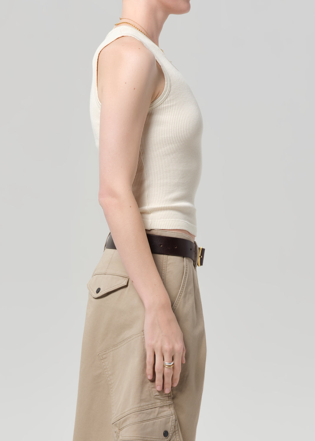 Person wearing a white sleeveless top and beige pants on a light gray background