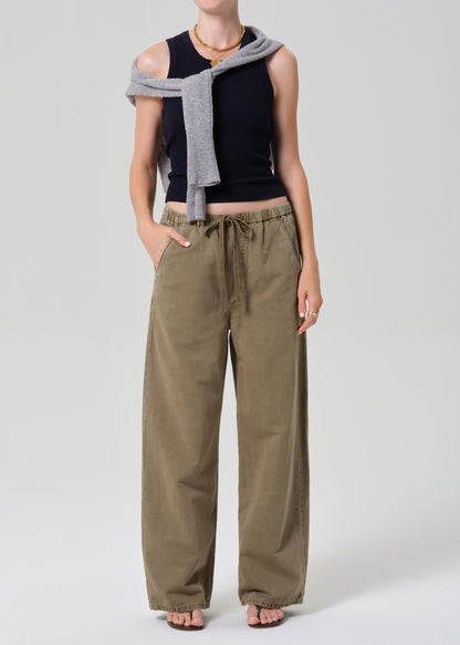 Person wearing a black sleeveless top, beige wide-leg pants, and a gray scarf on a white background