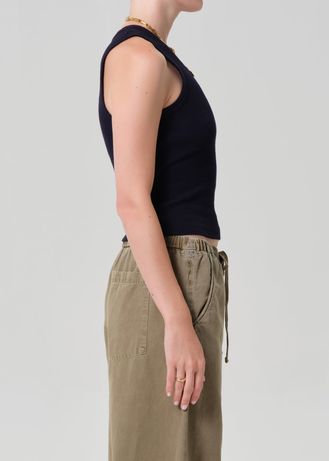 Person wearing a black sleeveless top and beige pants on a plain background