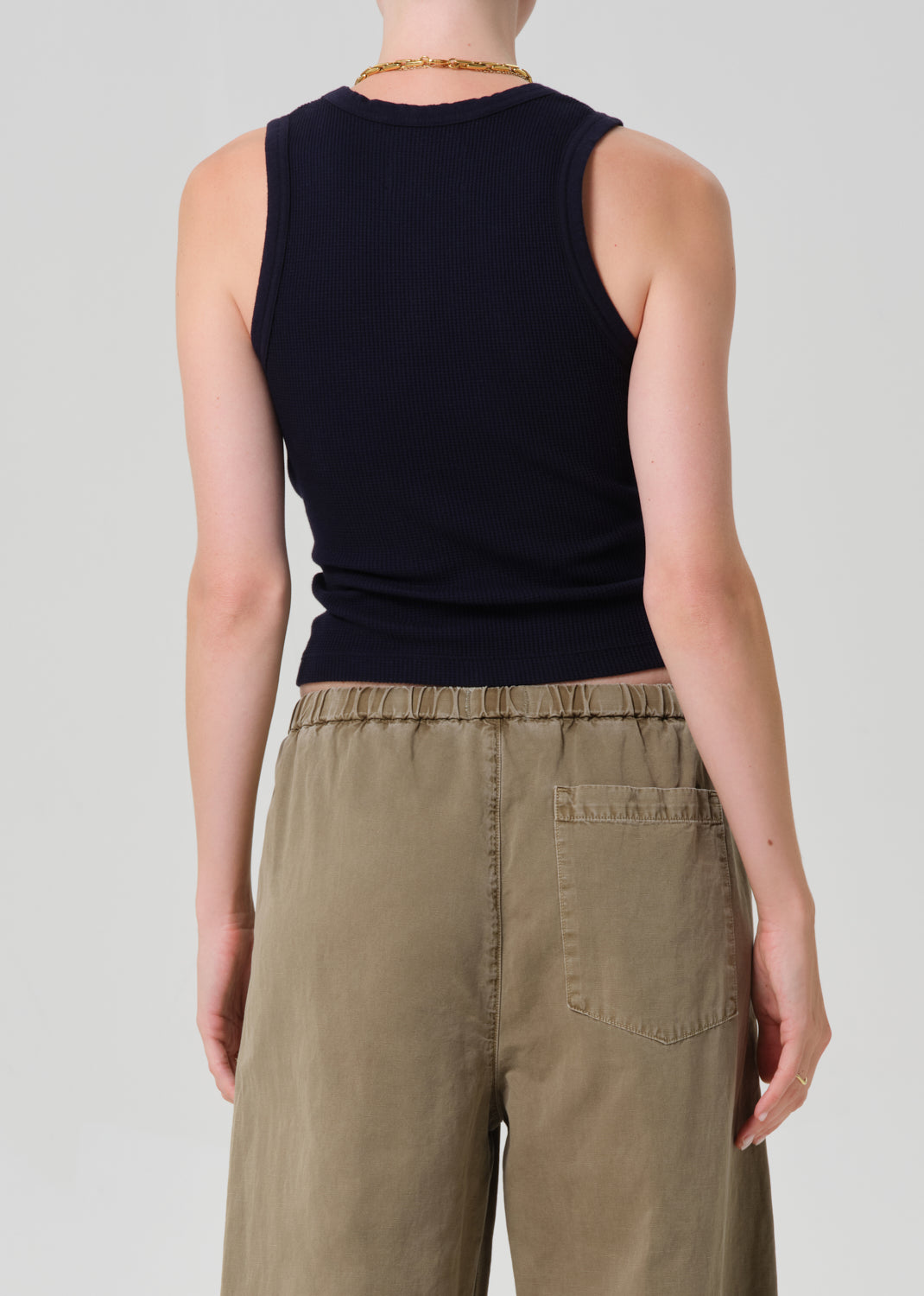 Person wearing a black sleeveless top and beige pants on a plain background