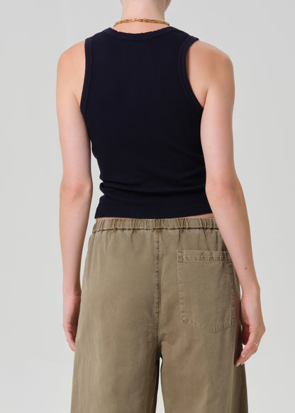 Person wearing a black sleeveless top and beige pants on a plain background