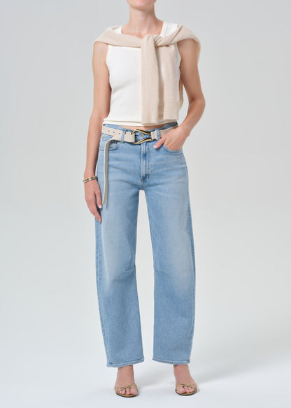 Person wearing a white tank top and light blue jeans with a belt on a gray background