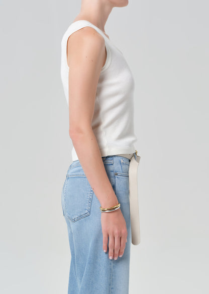 Person wearing a white tank top and light blue jeans with a belt on a gray background