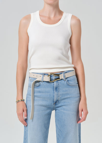 Person wearing a white tank top and light blue jeans with a belt on a gray background