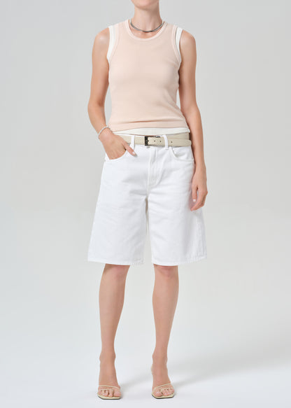 Person wearing a pink sleeveless top and white shorts on a plain background