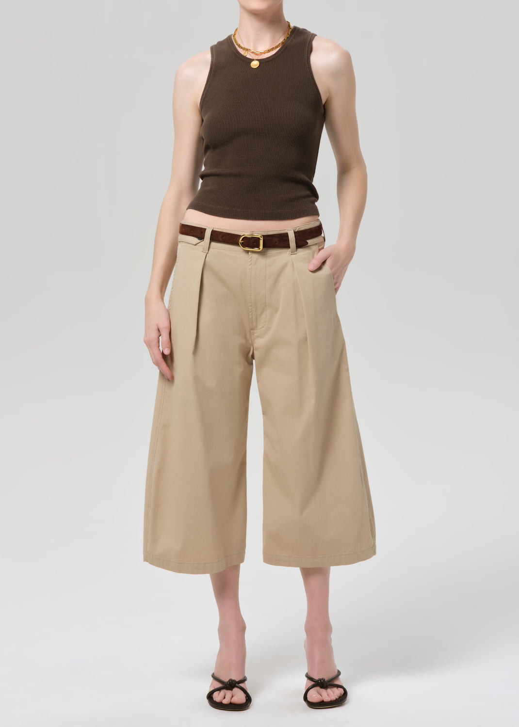 Person wearing a brown sleeveless top and beige wide-leg pants on a grey background