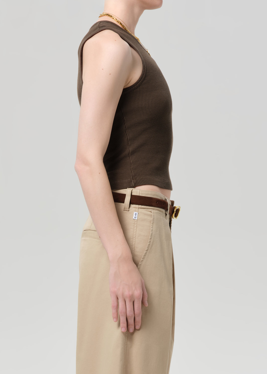 Person wearing a brown sleeveless top and beige pants on a light gray background