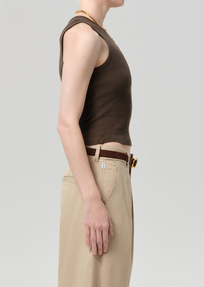 Person wearing a brown sleeveless top and beige pants on a light gray background