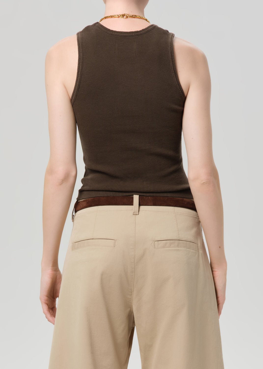 Person wearing a brown ribbed tank top and beige pants on a plain background