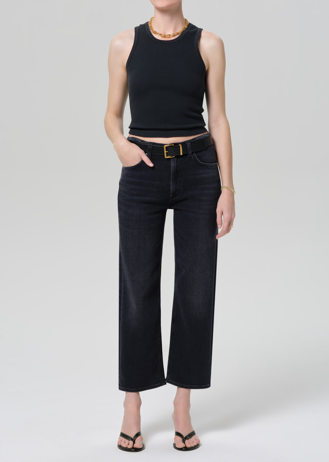 Person wearing a black tank top and black jeans on a grey background