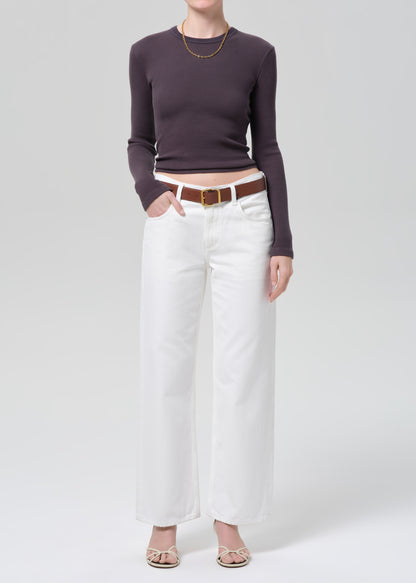 Person wearing a charcoal long-sleeve top and white jeans with a brown belt on a plain background