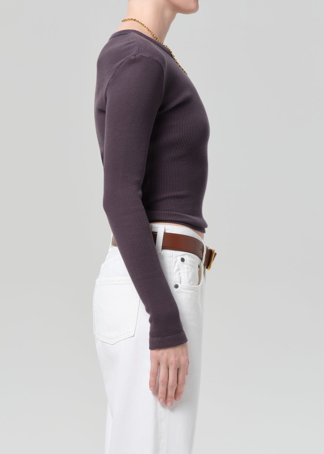 Person wearing a charcoal long-sleeve top and white jeans with a brown belt on a plain background