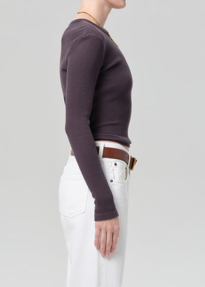Person wearing a charcoal long-sleeve top and white jeans with a brown belt on a plain background