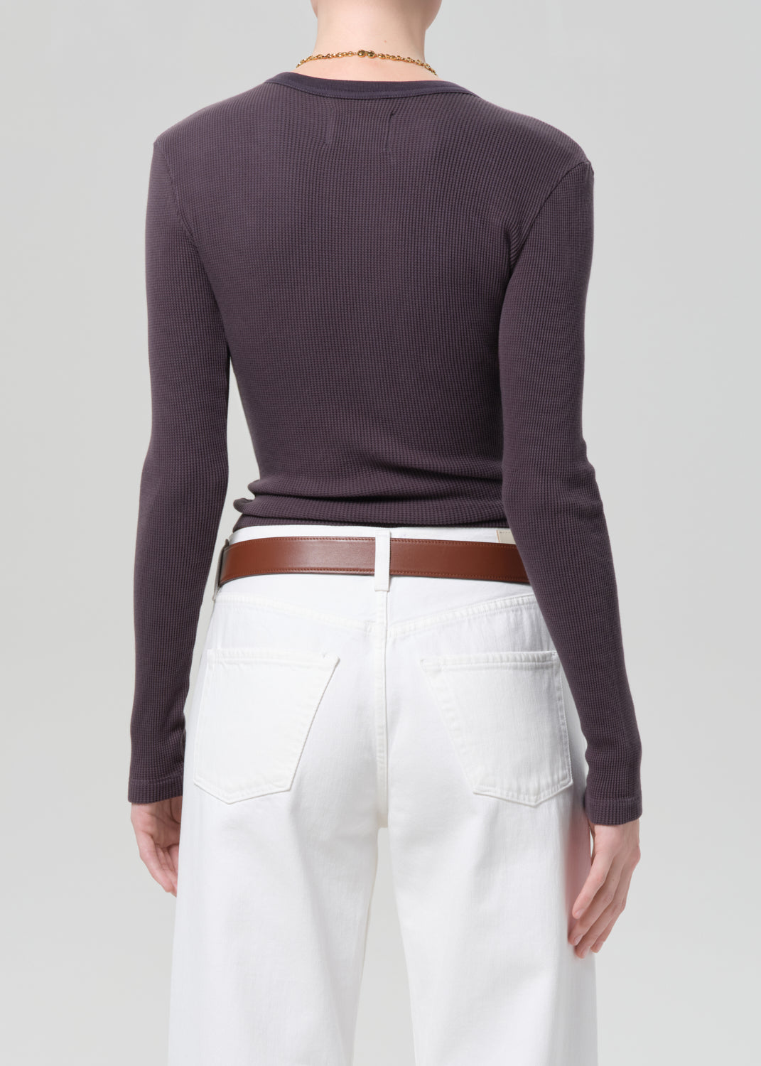 Person wearing a charcoal long-sleeve top and white jeans with a brown belt on a plain background