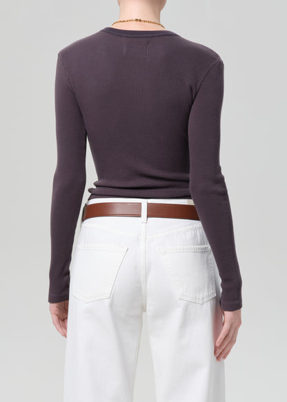 Person wearing a charcoal long-sleeve top and white jeans with a brown belt on a plain background