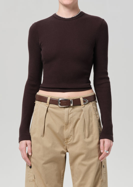 Person wearing a brown long-sleeve top and beige pants on a light gray background