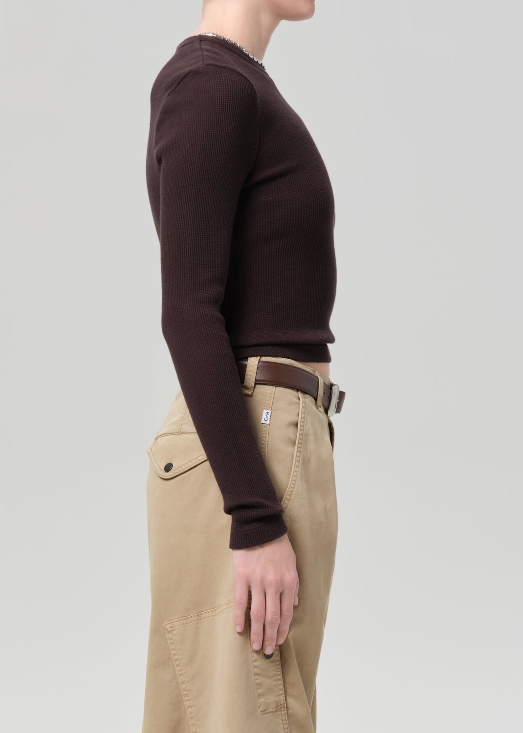 Person wearing a brown long-sleeve shirt and beige pants on a light gray background