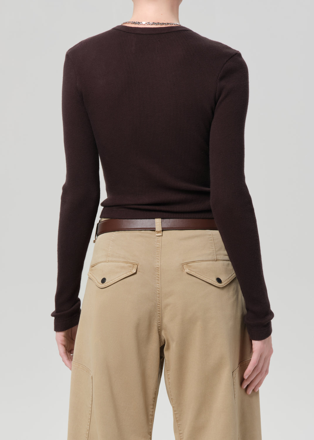 Person wearing a brown long-sleeve top and beige pants on a plain background