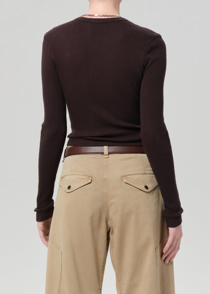Person wearing a brown long-sleeve top and beige pants on a plain background