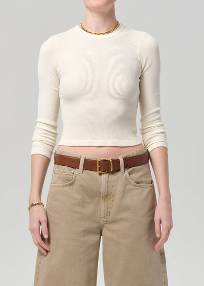 Person wearing a cream long-sleeve top and beige pants with a brown belt on a gray background