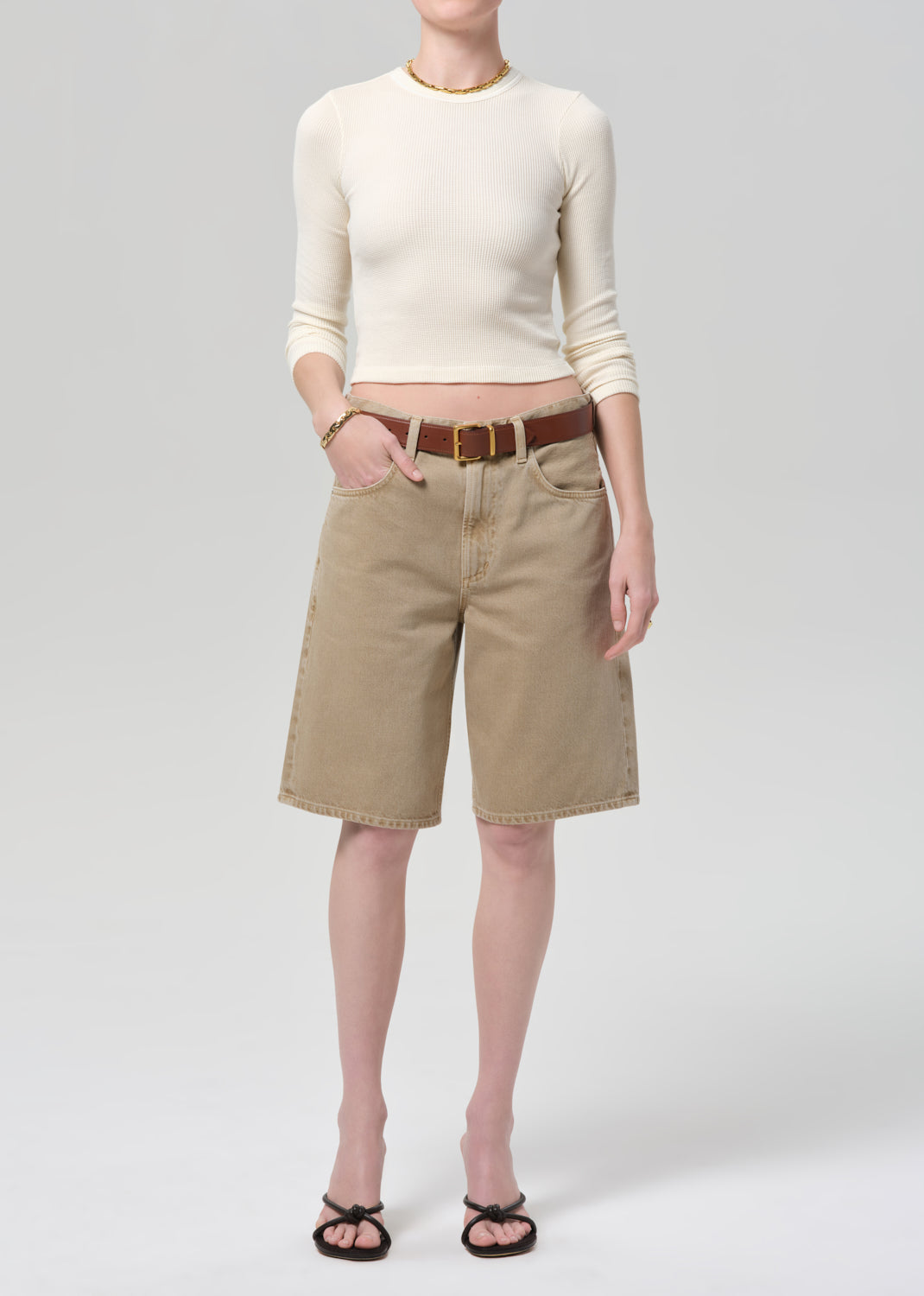 Person wearing a cream top and beige shorts on a plain background