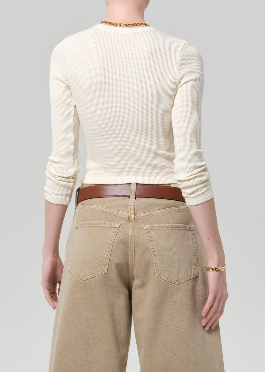 Person wearing a cream top and beige pants on a gray background