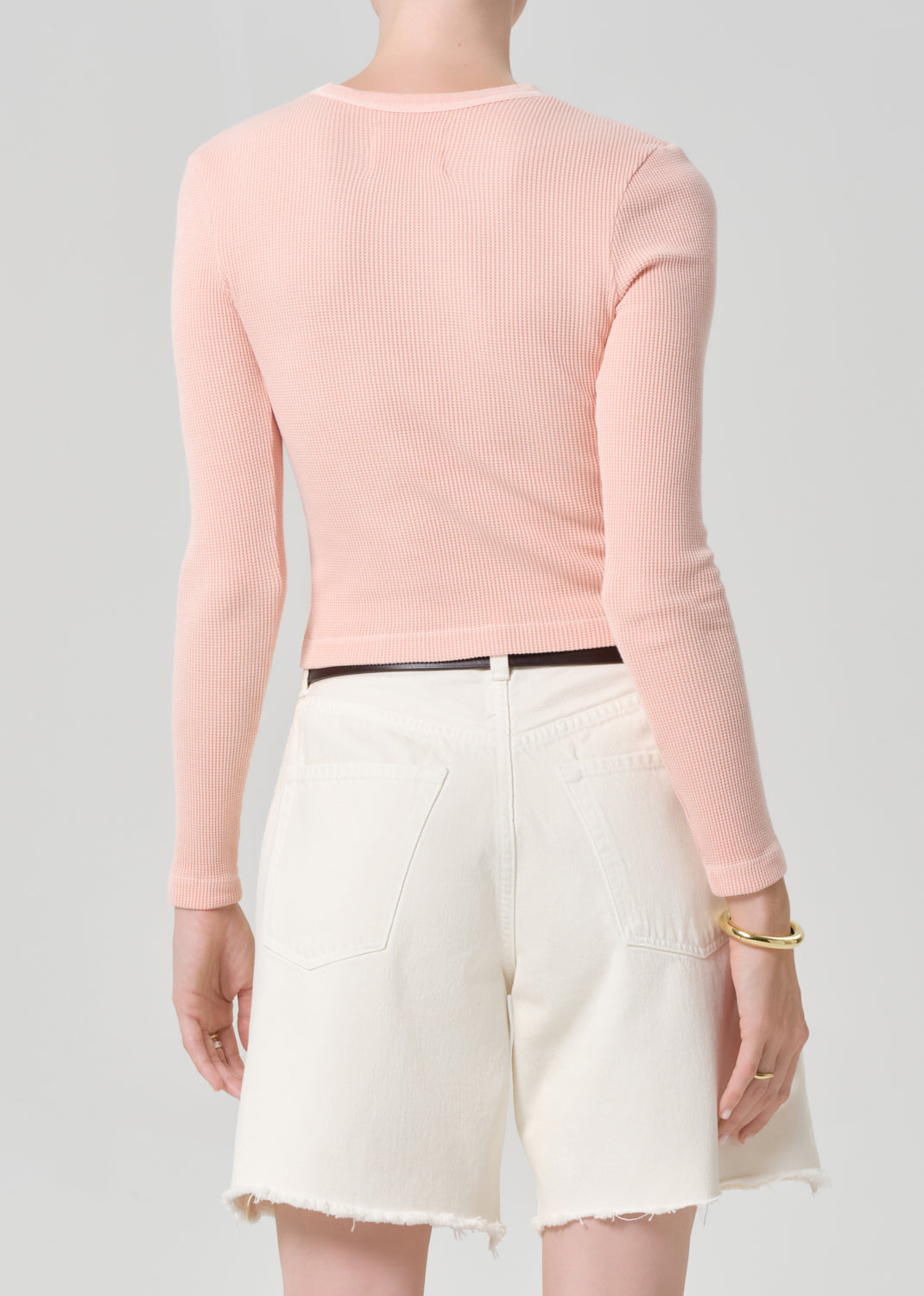 Person wearing a pink top with cream denim shorts