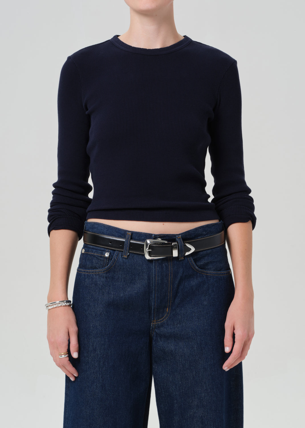 Person wearing a navy long-sleeve top and blue jeans on a plain background