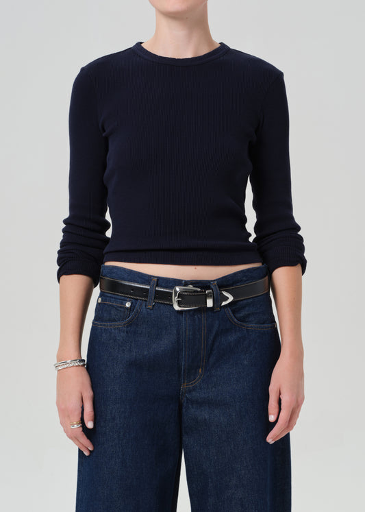 Person wearing a navy long-sleeve top and blue jeans on a plain background