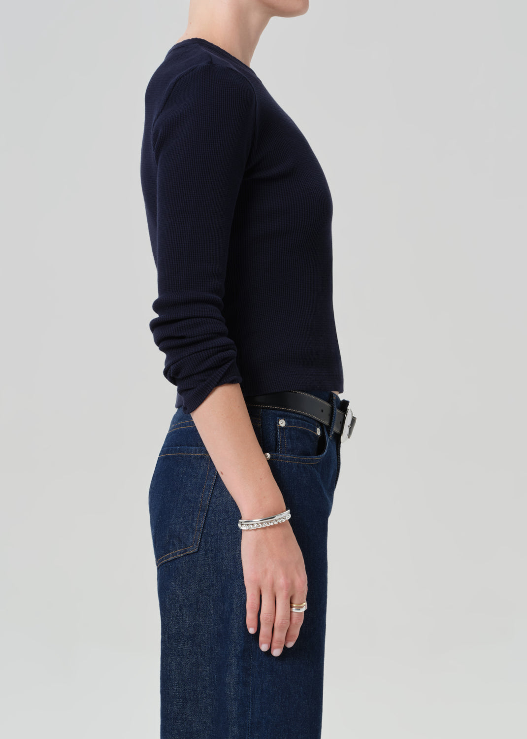 Person wearing a navy long-sleeve top and blue jeans on a plain background