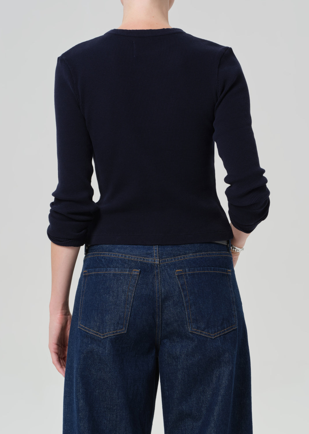 Person wearing a navy long-sleeve top and blue jeans on a plain background