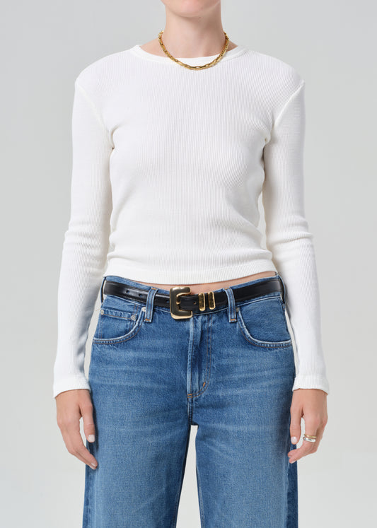 Person wearing a white long-sleeve top and blue jeans with a gold belt on a gray background